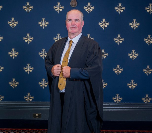 A man standing wearing a graduation gown