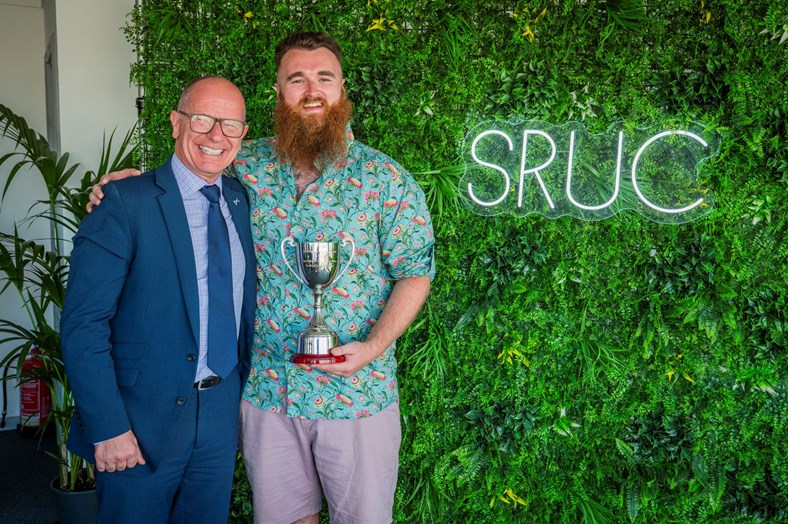 Two men smiling, one holding a trophy