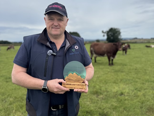 A man standing in a field with cows holding an award