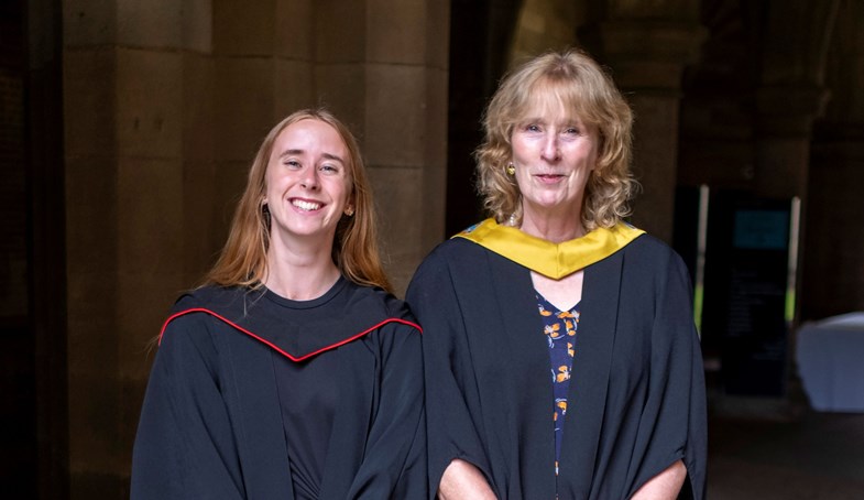 Two women in graduation gowns, smile for the camera