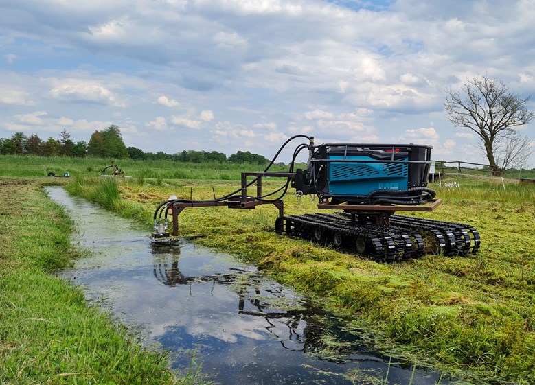 Robot at water's edge, on a farm with robotic arm extended into the water.