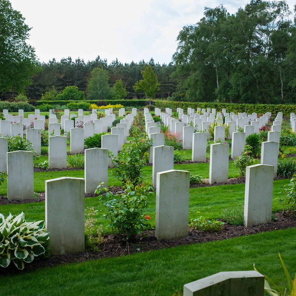 Cemetary full of uniform gravestones surrounded by lush foliage