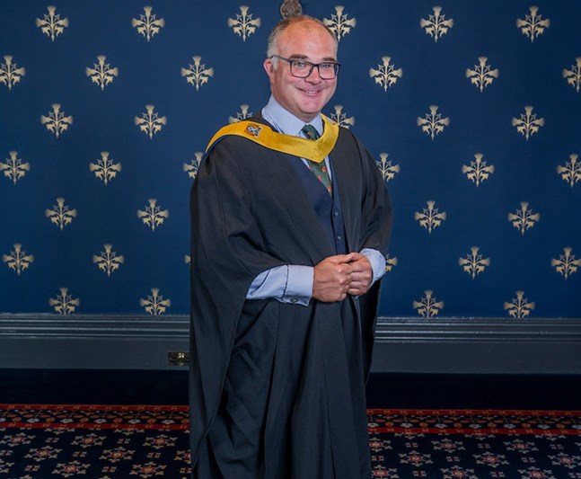 A man standing wearing a graduation gown