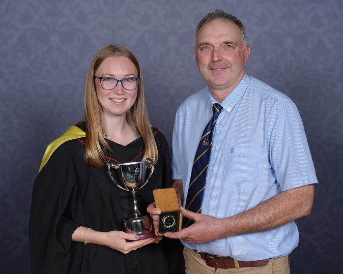 A girl in a graduation gown receiving a trophy from a man in a short and tie
