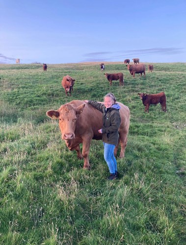 Katrina standing in a field with a cow and cows in the background