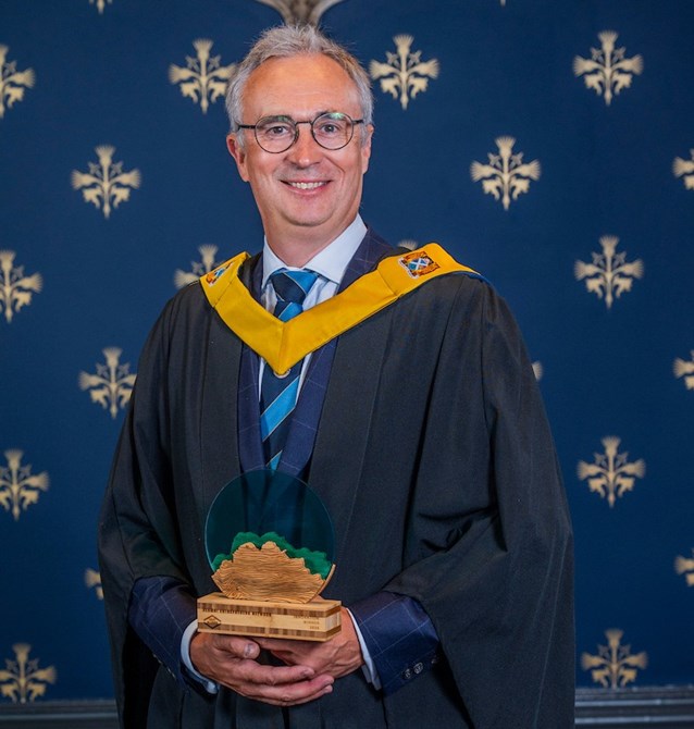 A man wearing a graduation gown holding an award
