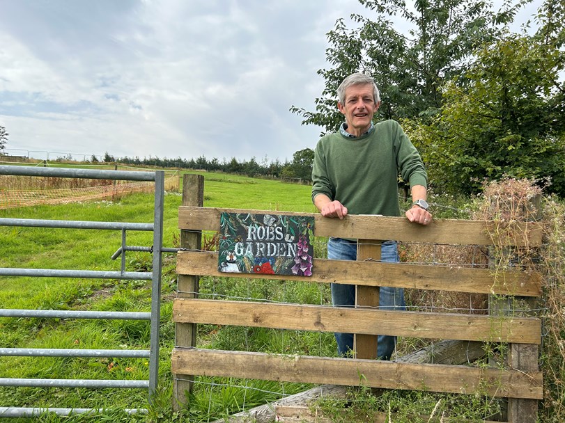 Man standing in front of a fence with the sign 'ROB'S GARDEn'